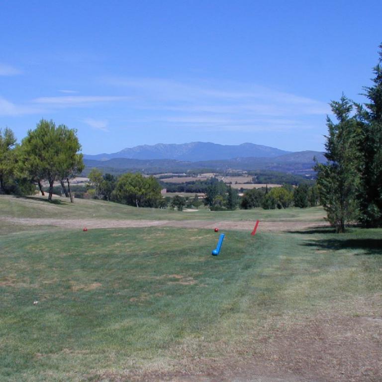 Panoramaaufnahme eines Golfplatzes mit Blick auf eine Bergkette unter blauem Himmel.