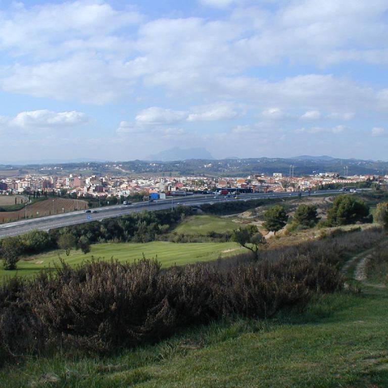 Panoramaaufnahme einer städtischen Landschaft, die durch eine Schnellstraße und eine bergige Kulisse im Hintergrund gekennzeichnet ist.