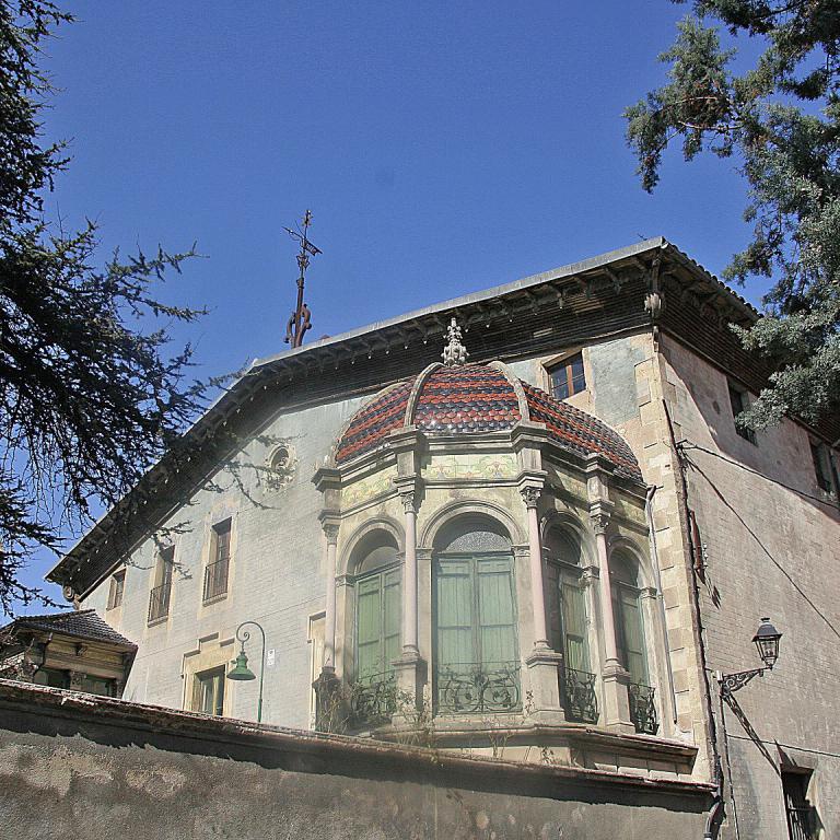 Eine historische Villa mit einem verzierten Eingangsbereich, umrahmt von Bäumen unter blauem Himmel.