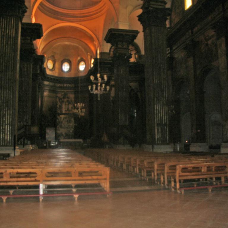Der Innenraum einer großen Kirche mit langen Reihen von Holzbänken und massiver Säulenarchitektur.