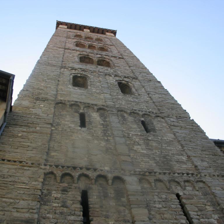 Der historische, steinverkleidete Glockenturm einer Kirche, der sich unter einem klaren blauen Himmel erhebt.
