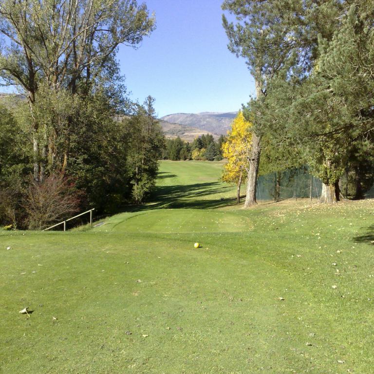 Eine weite Aufnahme eines Golfplatzes mit sattgrünem Rasen, umgeben von Bäumen und einem Blick auf die Berge.