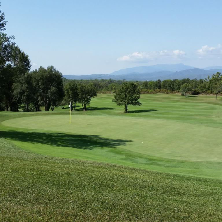 Eine weite Aufnahme eines Golfplatzes mit sattgrünen Fairways, umgeben von Bäumen und im Hintergrund blauen Bergen.