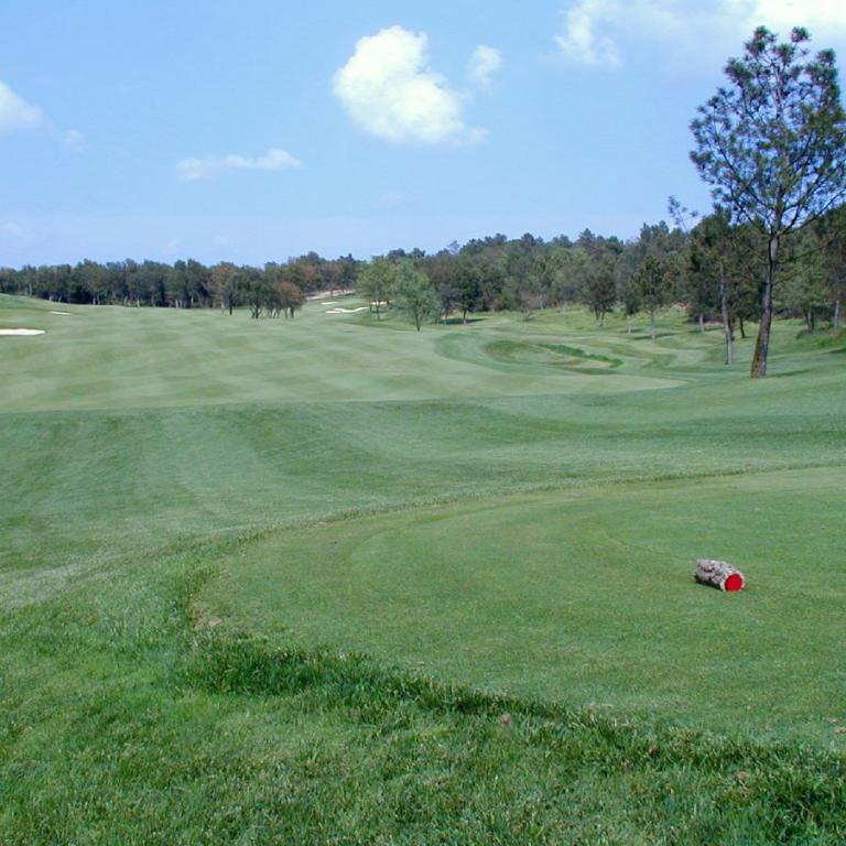 Panoramaaufnahme eines weitläufigen und gut gepflegten Golfplatzes unter blauem Himmel.