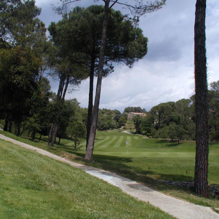 Ein Weg führt durch ein gepflegtes Golfgelände, umgeben von hohen Bäumen und grüner Wiese.