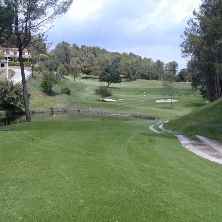 Eine weitläufige und gepflegte Golflandschaft mit einem Teich im Vordergrund und einem gewundenen Weg.
