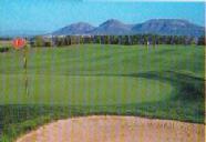 Panoramablick auf einen Golfplatz mit Sandbunker im Vordergrund und sanften Bergen im Hintergrund.