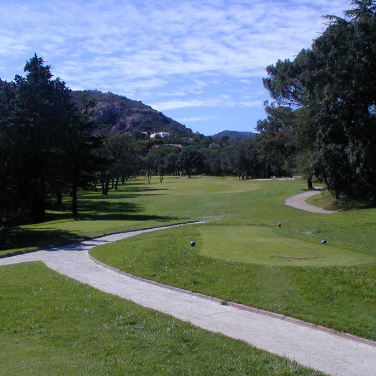 Ein Blick auf einen weitläufigen Golfplatz mit grünen Rasenflächen und umgebenden Bäumen unter blauem Himmel.