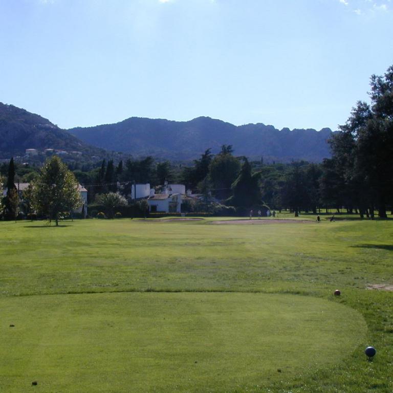 Eine weite Aufnahme eines gepflegten Rasens, der wie ein Golfplatz wirkt, mit bewaldeten Hügeln im Hintergrund.