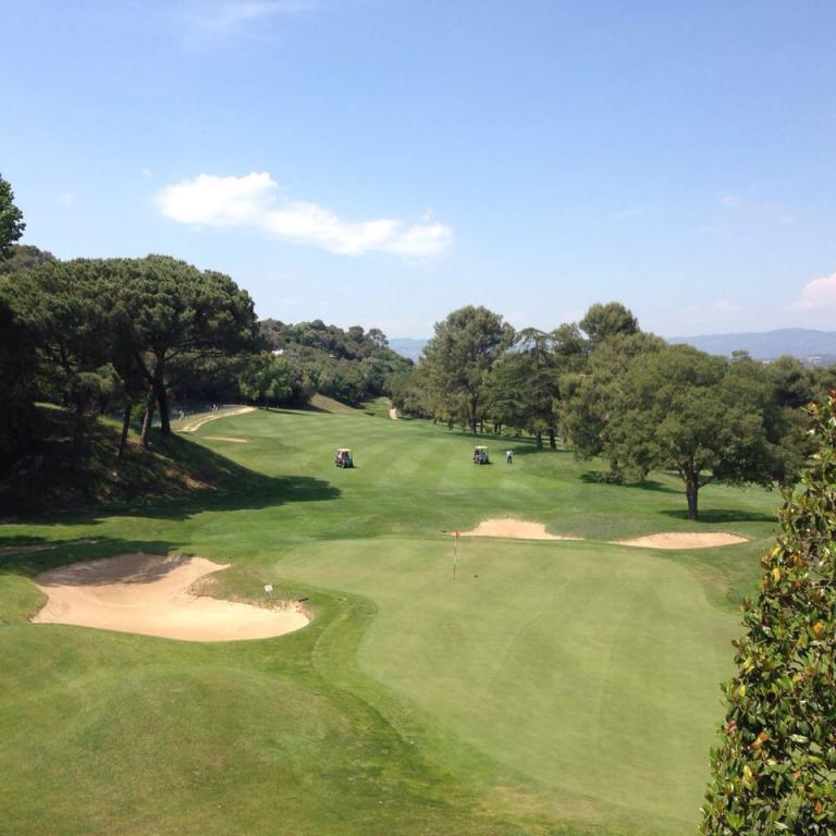 Panoramablick über einen gepflegten Golfplatz, der von Bäumen umgeben ist und unter einem klaren blauen Himmel liegt.