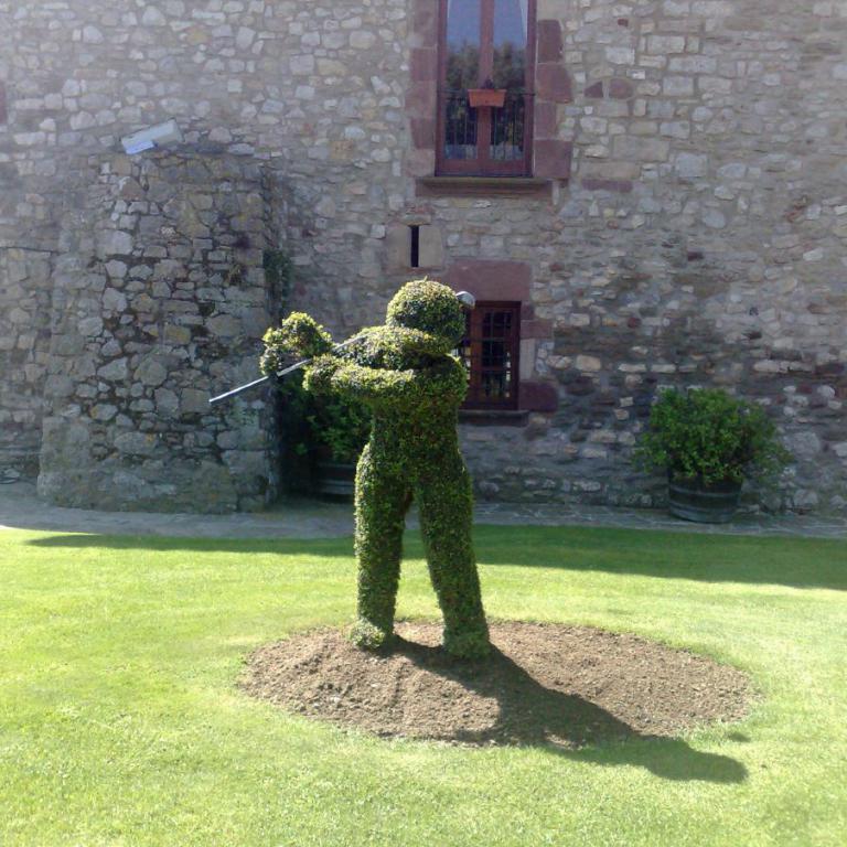 Eine große Topiary-Statue eines Mannes in einem Garten vor einer Steinmauer.