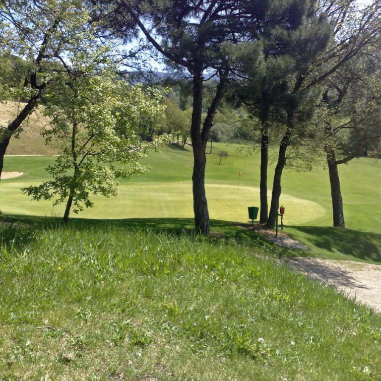 Aussicht auf einen Golfplatz, umrahmt von Bäumen und Wiesen.