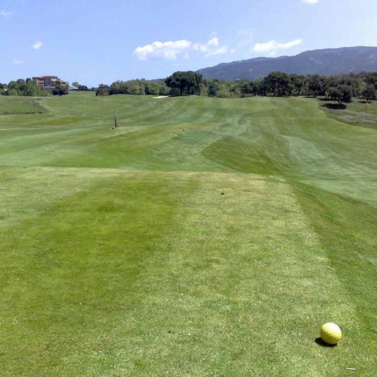 Ein Golfplatz mit einem Gelb-Golfball im Vordergrund vor einer hügeligen Landschaft.