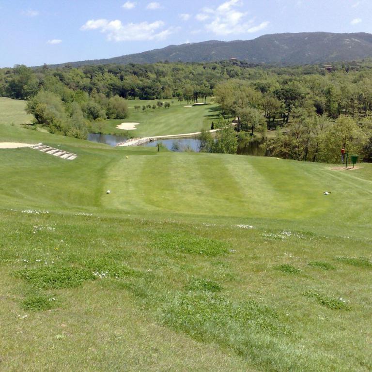 Weitläufige Aufnahme eines Golfplatzes mit grünem Fairway und Hintergrund von bewaldeten Hügeln unter blauem Himmel.