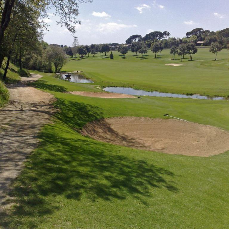 Eine weite Szenerie eines Golfplatzes mit Grünflächen, einem Wasserlauf und einem Sandbunker im Vordergrund.