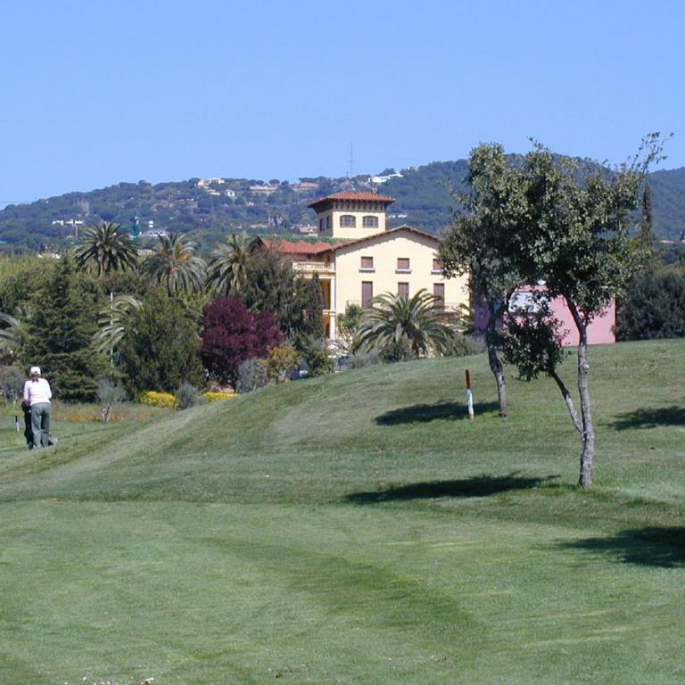 Blick über eine grüne Rasenfläche auf ein mediterranes Anwesen mit Hügeln im Hintergrund.