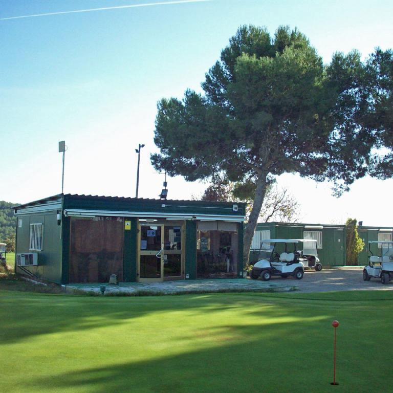 Ein Golfclubhaus auf einer großen, grünen Rasenfläche, umgeben von Bäumen unter einem klaren Himmel.