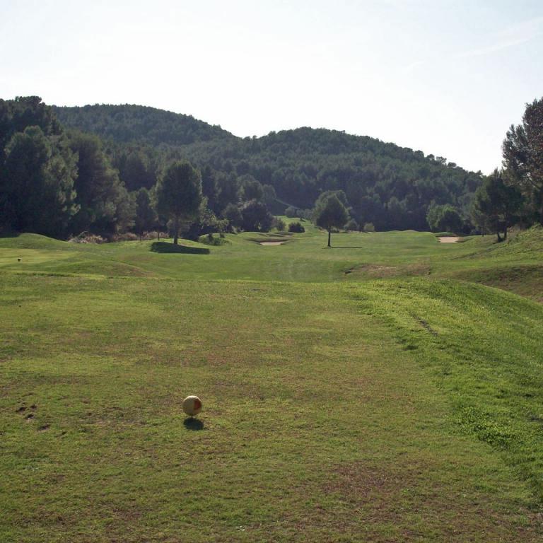 Weitläufiger Golfplatz mit einem Golfball im Vordergrund und einer Kulisse aus bewaldeten Hügeln im Hintergrund.