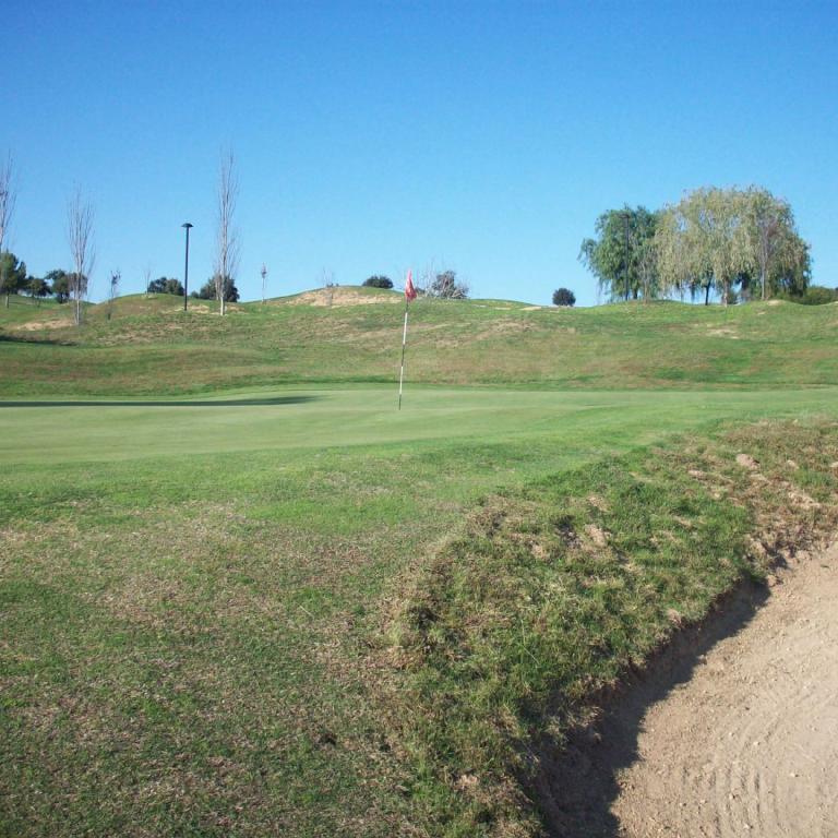 Panoramaaufnahme eines weitläufigen Golfplatzes mit grünem Rasen und Sandbunkern unter blauem Himmel.