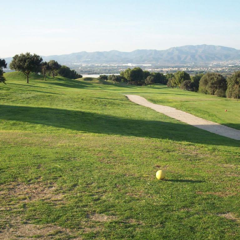 Ein Golfplatz mit einem Weg, der durch die grüne Wiese führt, und im Hintergrund eine weite Aussicht auf eine Stadt und Berge.