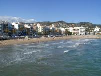 Eine Aufnahme eines belebten Küstenortes mit einem breiten Sandstrand und Reihen von Gebäuden unter einem blauen Himmel.