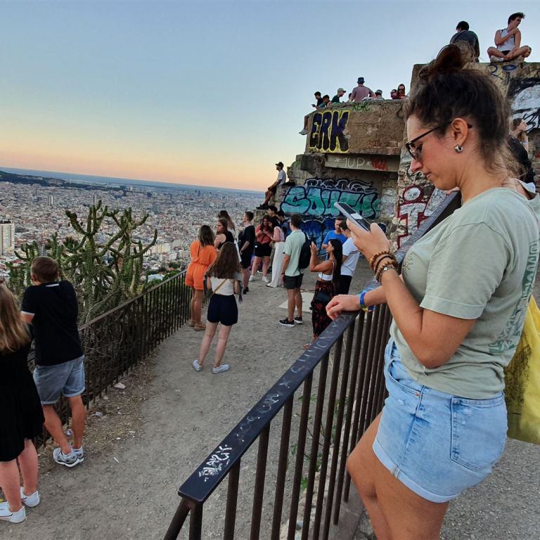Eine Gruppe von Menschen steht auf einem Dach und blickt bei Sonnenuntergang auf die ausgedehnte Skyline einer Großstadt.