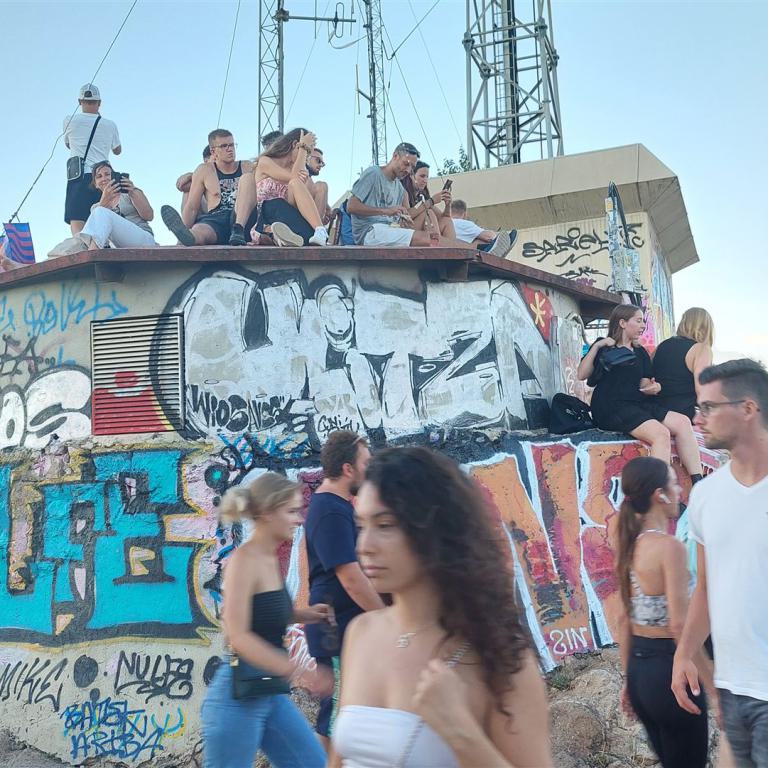 Eine Gruppe junger Leute sitzt und steht auf einem Dach, das komplett mit bunten Graffiti bedeckt ist. Die Aufnahme wurde bei Dämmerung gemacht.