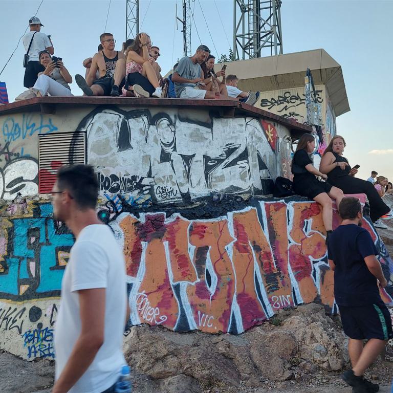 Eine Gruppe von Menschen sitzt und steht auf einer stark mit Graffiti bedeckten Betonplattform bei Sonnenuntergang.