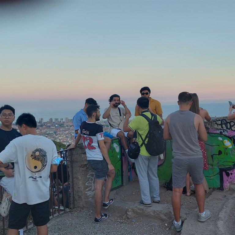 Eine große Gruppe von Menschen beobachtet bei Sonnenuntergang einen weiten Stadtpanoramaausblick.