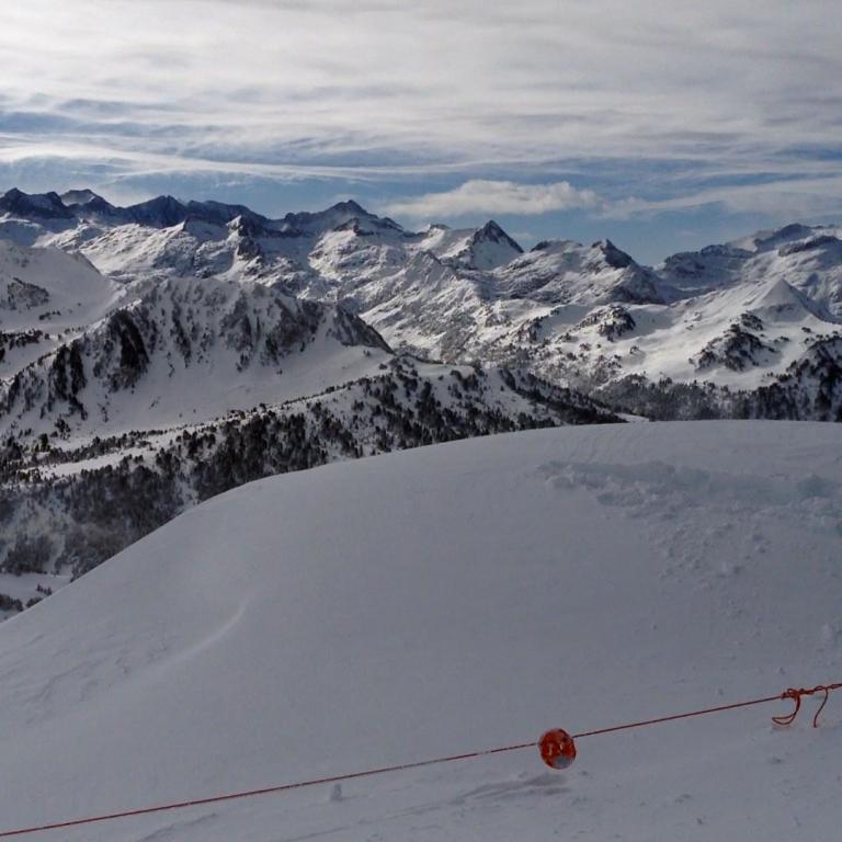 Weitwinkelaufnahme einer verschneiten Berglandschaft mit majestätischen Gipfeln und einem sanft abfallenden Hang im Vordergrund.