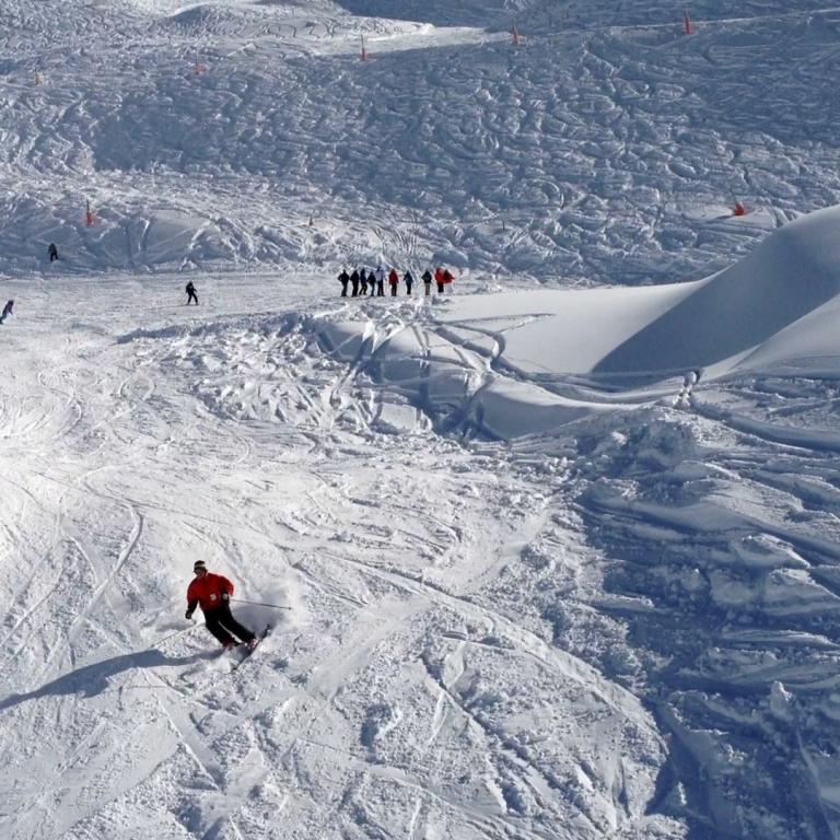 Panoramablick auf einen weiten, verschneiten Skihang mit Sessellift und Skifahrern.