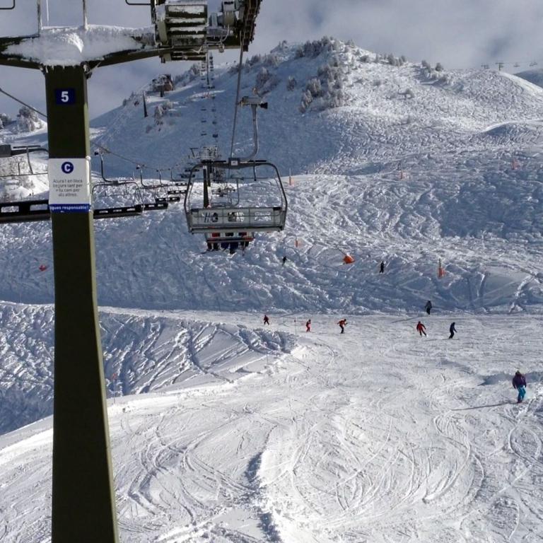 Ein Panorama von einer Skipiste mit einem beleuchteten Sessellift im Vordergrund und verschneiten Berghängen im Hintergrund.