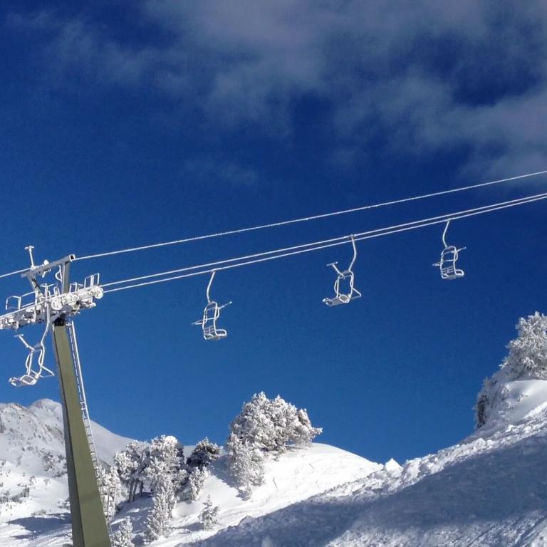 Ein Skilift fährt über einen weiten, schneebedeckten Berghang unter blauem Himmel.