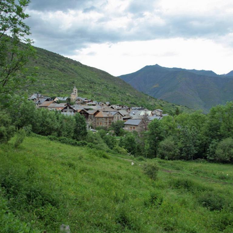 Ein Dorf in einem tiefgrünen Tal, umgeben von steilen, bewaldeten Berghängen.