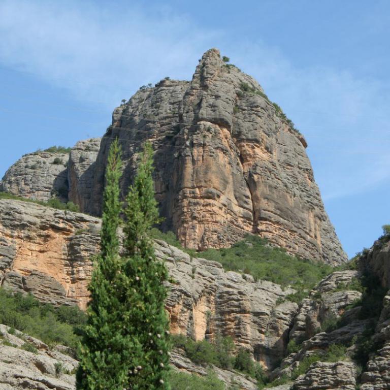 Ein Panorama von großen, geschichteten Felsformationen, die vor einem blauen Himmel aufragen und von grüner Vegetation umgeben sind.