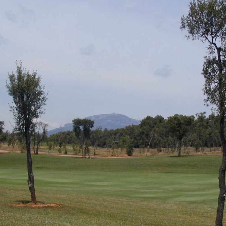 Panoramablick auf einen Golfplatz mit bewaldetem Mittelgrund und Bergen im Hintergrund