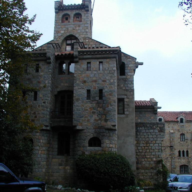 Ein großes, historisches Gebäude aus Steinmauerwerk mit charakteristischen Türmchen und Fenstern, umrahmt von Bäumen.